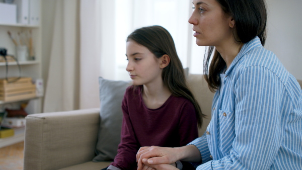 Sad and depressed small girl with mother indoors having therapy appointment, mental health concept.