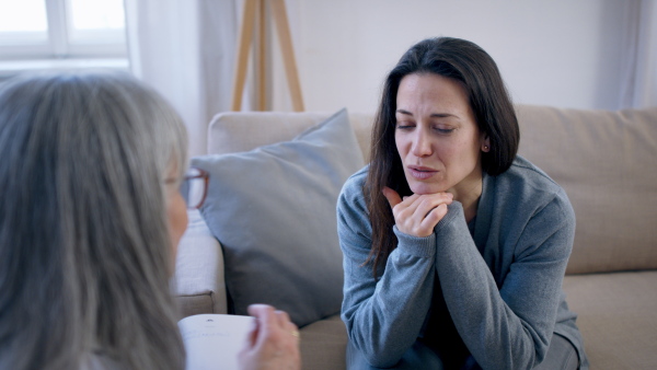 Sad and depressed young woman talking to psychotherapist indoors, mental health concept.