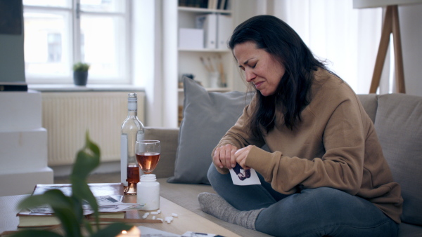 Depressed woman with alcohol indoors, tearing photograph. Mental health concept.