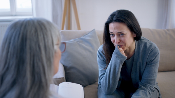 Sad and depressed young woman talking to psychotherapist indoors, mental health concept.