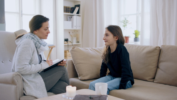 Sad and depressed small girl talking to psychotherapist indoors, mental health concept.