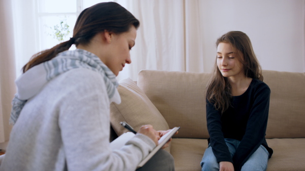 Sad and depressed small girl talking to psychotherapist indoors, mental health concept.