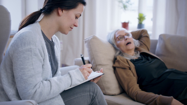 Sad and depressed senior woman talking to psychotherapist indoors, mental health concept.