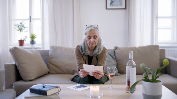 Front view of depressed woman looking at photographs indoors, mental health concept.