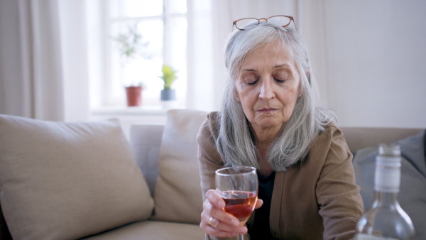 Front view of depressed woman pouring wine indoors, mental health concept.