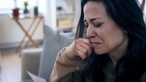 Crying depressed woman sitting and looking at photograph indoors, mental health concept.