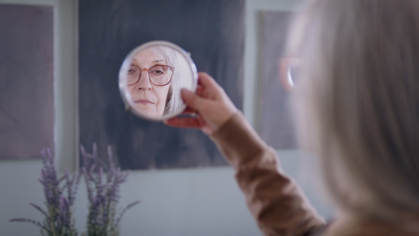 Sad and depressed senior woman looking in mirror indoors, mental health concept.