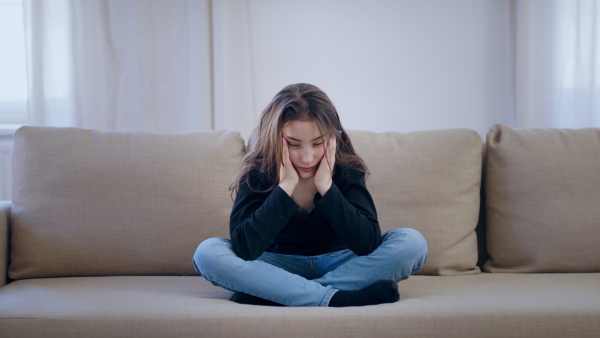 Front view of sad and depressed small girl sitting indoors, mental health concept.