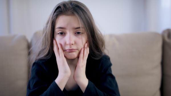 Front view of sad and depressed small girl sitting indoors, mental health concept.