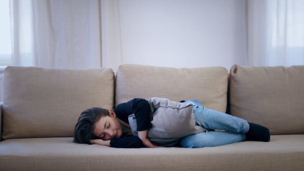 Front view of sad and depressed small girl lying on sofa indoors, mental health concept.