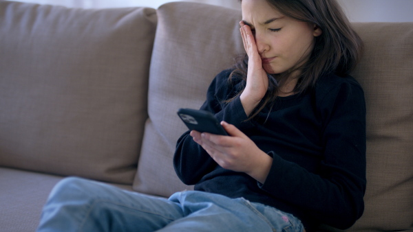 Sad and depressed small girl using smartphone indoors, mental health concept.