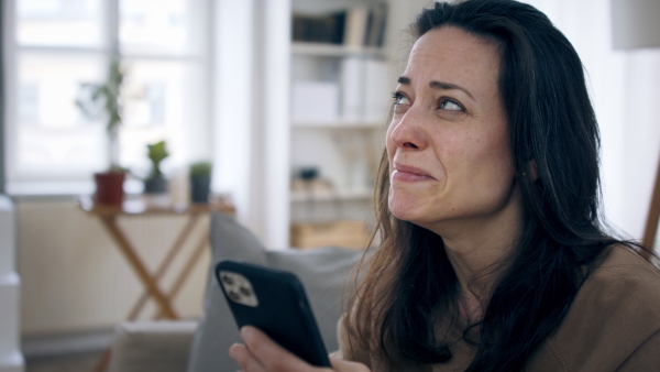 Crying sad and depressed woman looking at smartphone indoors, mental health concept.