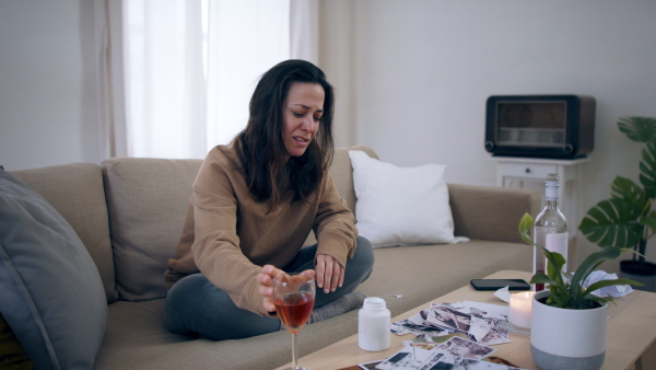 Crying depressed woman with pills and alcohol indoors, mental health concept.