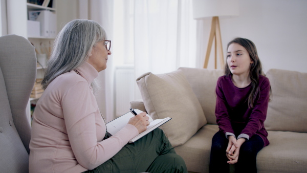 Sad and depressed small girl talking to psychotherapist indoors, mental health concept.