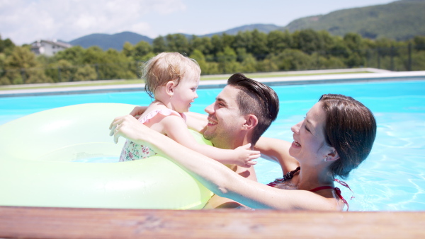 Happy young family with small daughter in swimming pool outdoors in backyard garden.