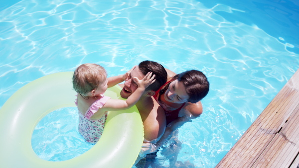 Happy young family with small daughter in swimming pool outdoors in backyard garden.