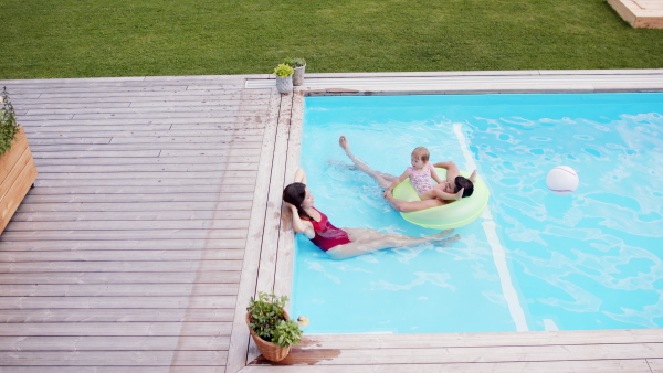 Top view of happy young family with small daughter in swimming pool outdoors in backyard garden.