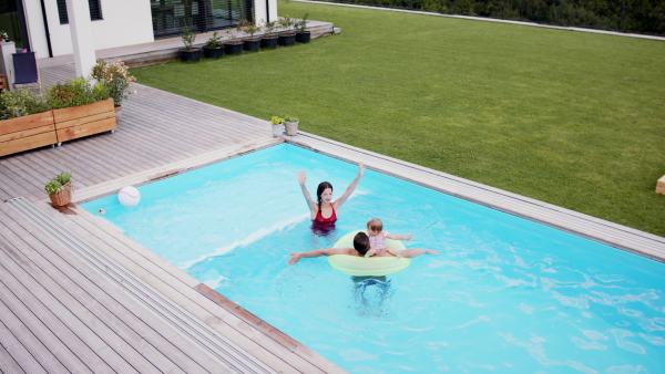 Top view of happy young family with small daughter in swimming pool outdoors in backyard garden, looking at camera.