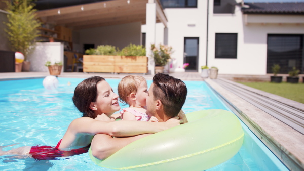 Happy young family with small daughter in swimming pool outdoors in backyard garden.