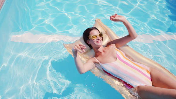 Young woman with sunglasses in swimming pool outdoors in backyard garden, relaxing.