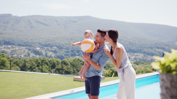 Portrait of young family with small daughter outdoors in backyard garden, playing with ball.