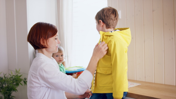 Mother with three small children in hall in the morning at home, getting ready for school.