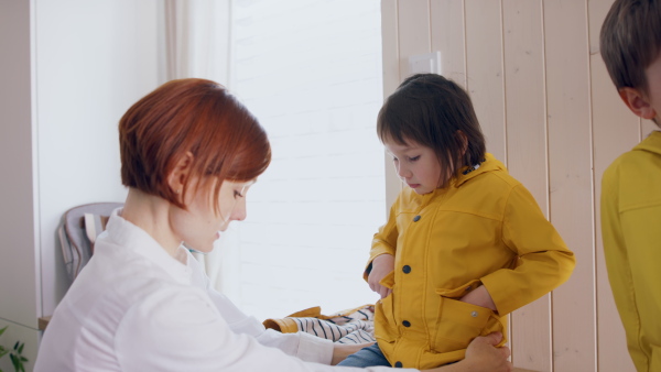 Mother with three small children in hall in the morning at home, getting ready for school.