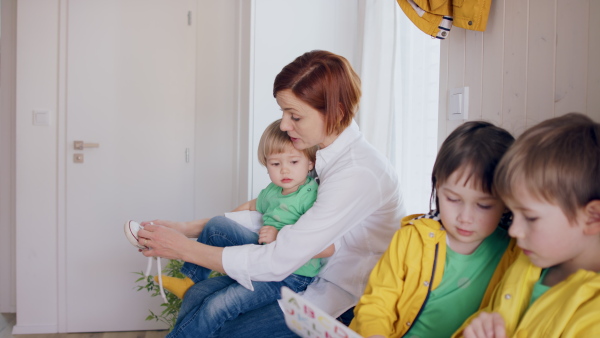 A mother with small children in hall in the morning at home, putting on shoes.