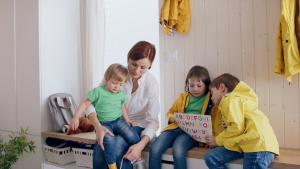 A mother with small children in hall in the morning at home, putting on shoes.