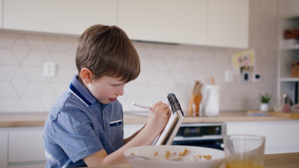 A small boy in kitchen in the morning at home, writing in personal organiser.