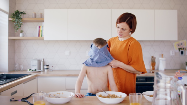 Mother with small children in kitchen in the morning at home, getting dressed when eating breakfast.