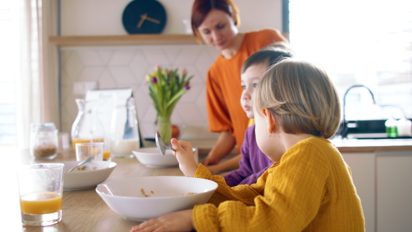 Busy mother with small children in kitchen in the morning at home, eating breakfast.