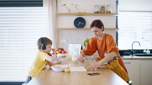 Busy mother with small children in kitchen in the morning at home, eating breakfast.