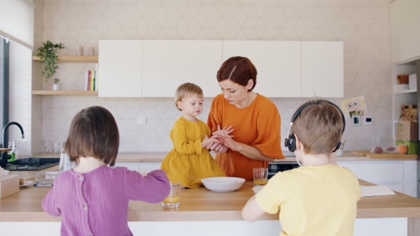 Busy mother with small children in kitchen in the morning at home, eating breakfast.