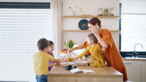 Busy mother with small children in kitchen in the morning at home, using smartphone when eating breakfast.