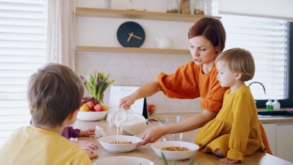 Busy mother with small children in kitchen in the morning at home, eating breakfast.