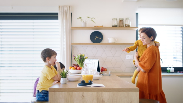 Busy mother with small children in kitchen in the morning at home, eating breakfast.