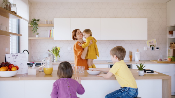 Happy mother with small children in kitchen in the morning at home, breakfast time.