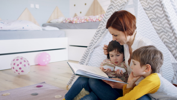 Mother with small children sitting in bedroom at home, reading story book.