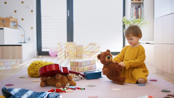 Happy small toddler girl sitting on floor in bedroom indoors at home, playing.