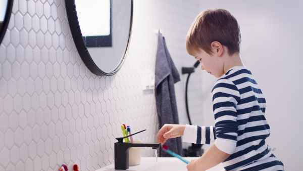 Small boy in pajamas in bathroom in the morning at home, brushing teeth.