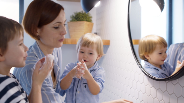 Mother with three small children in pajamas in the bathroom indoors at home, washing hands.