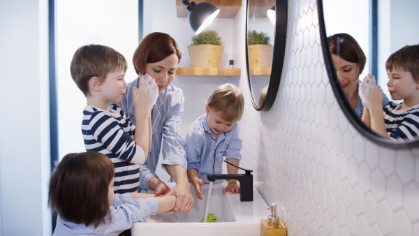 Mother with three small children in pajamas in the bathroom indoors at home, washing hands.