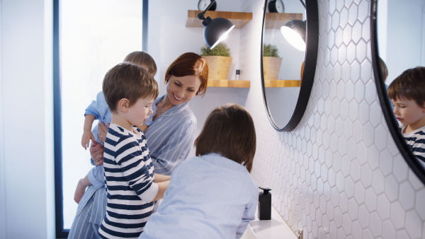 Mother with three small children in pajamas in the bathroom indoors at home, washing hands.