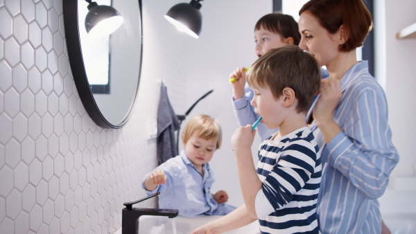 Mother with three small children in pajamas in the bathroom indoors at home, brushing teeth.