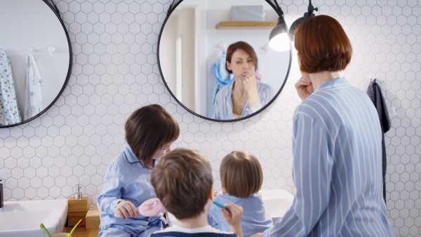 Mother with three small children in pajamas in the bathroom indoors at home, brushing teeth.