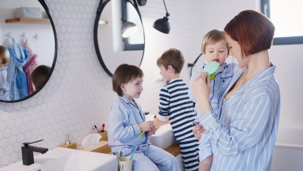 Mother with three small children in pajamas in the bathroom indoors at home, brushing teeth.