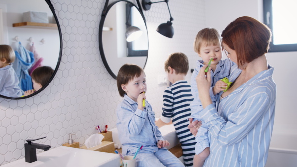 Mother with three small children in pajamas in the bathroom indoors at home, brushing teeth.