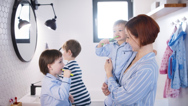 Mother with three small children in pajamas in the bathroom indoors at home, brushing teeth.