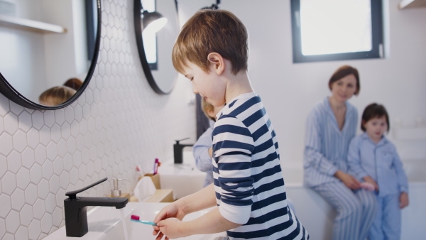 Mother with three small children in pajamas in the bathroom indoors at home, brushing teeth.